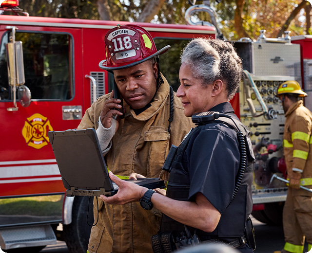 Fire fighter and police officer using smartphone and laptop on the scene
