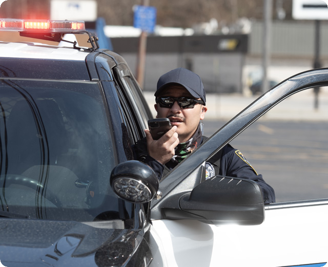 Police officer in cruiser using a FirstNet push-to-talk device on scene 