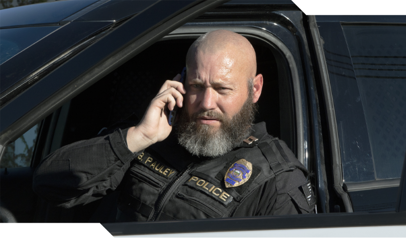 Police officer talking on mobile phone inside car.