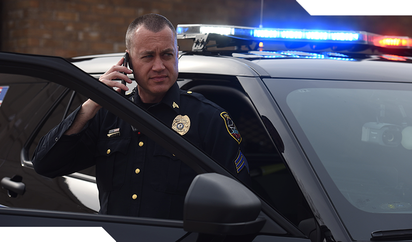 Police officer talking on mobile phone by police car.