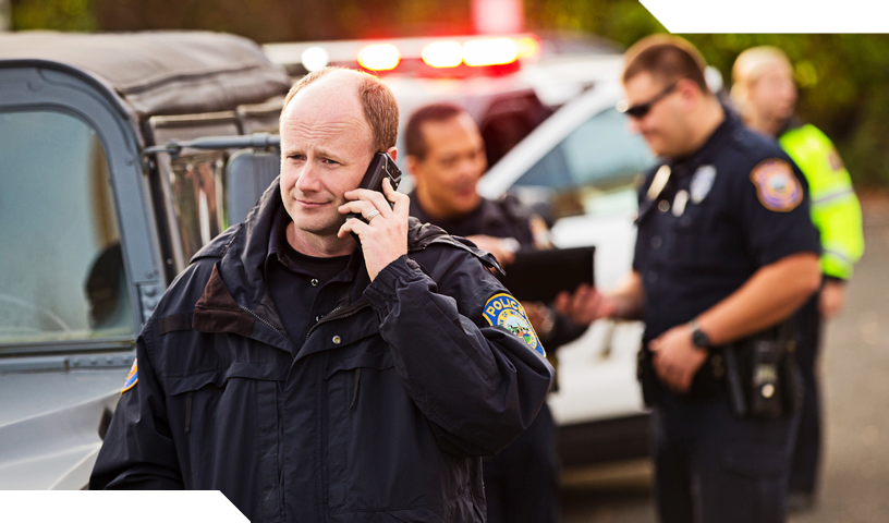 Police officer talking on mobile phone with police vehicles behind him.